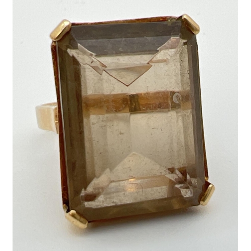 31 - An 18K gold cocktail ring set with a large emerald cut smoked quartz stone. In claw set mount with p... 