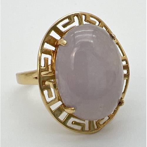 103 - A 14K gold dress ring set with a large oval cabochon of lavender jade. In a Greek key pierced work m... 