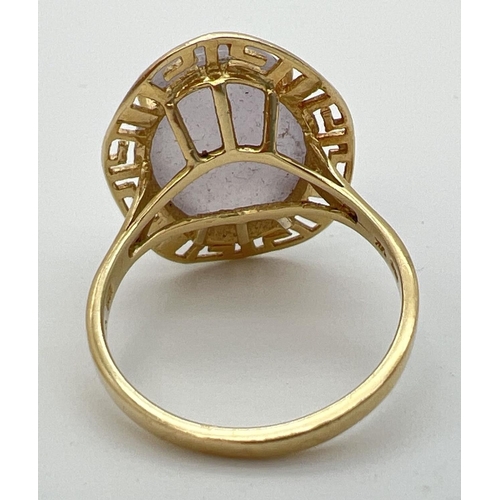 103 - A 14K gold dress ring set with a large oval cabochon of lavender jade. In a Greek key pierced work m... 