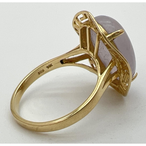 103 - A 14K gold dress ring set with a large oval cabochon of lavender jade. In a Greek key pierced work m... 