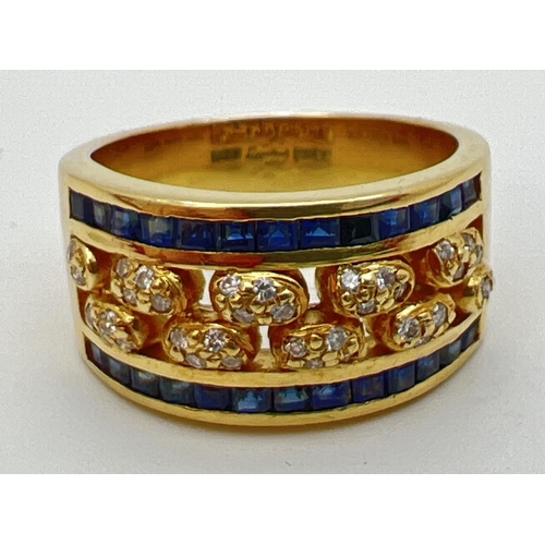 1138 - A gold open work sapphire and diamond band ring. 13 square cut bezel set sapphires to each side with... 