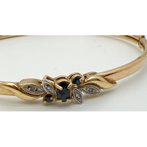 1031 - A gold sapphire and diamond set hinged bangle. Central oval cut sapphire with 2 small round cut sapp... 