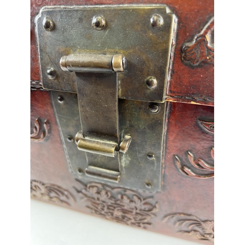 1288 - A vintage red leather trunk with Oriental floral & character relief design to front & sides. Drop me... 