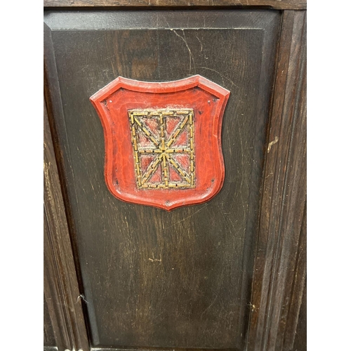 1366 - An antique dark wood high back settle bench with painted crest detail. Panelled back with carved Got... 