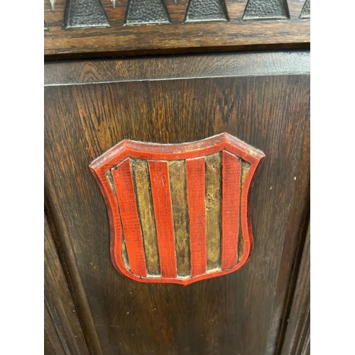 1366 - An antique dark wood high back settle bench with painted crest detail. Panelled back with carved Got... 