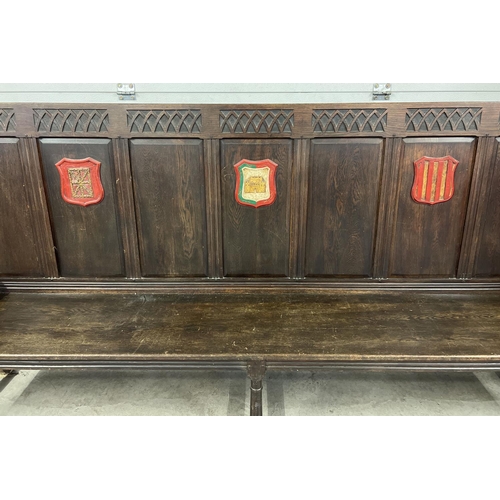 1366 - An antique dark wood high back settle bench with painted crest detail. Panelled back with carved Got... 