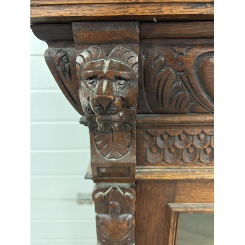 1367 - An antique dark wood wall hanging display cupboard with highly carved detail. With lion head finials... 