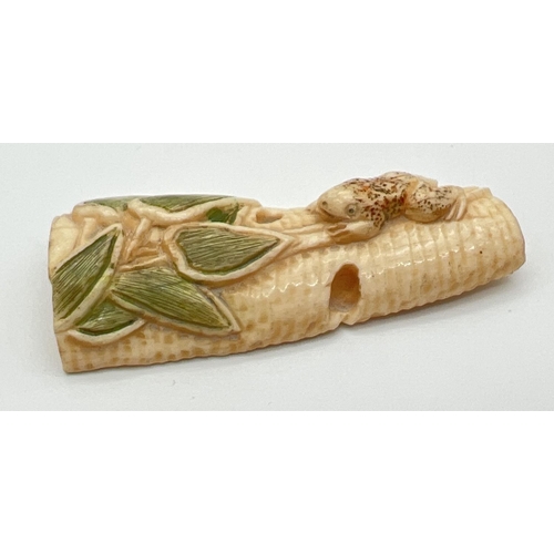 1245 - A carved netsuke in the form of a tree frog climbing a tree trunk. With coloured detail to leaves an... 