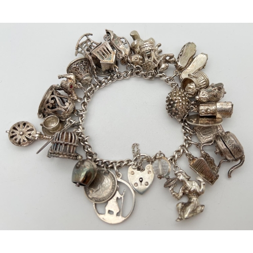 1004 - A vintage silver charm bracelet with padlock, safety chain and 27 silver and white metal charms. Man... 