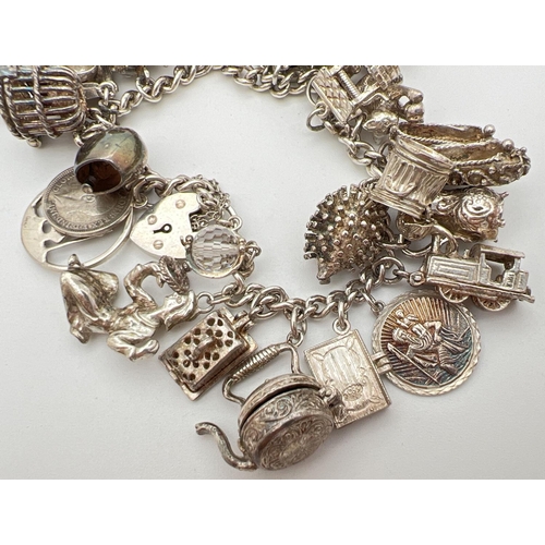 1004 - A vintage silver charm bracelet with padlock, safety chain and 27 silver and white metal charms. Man... 