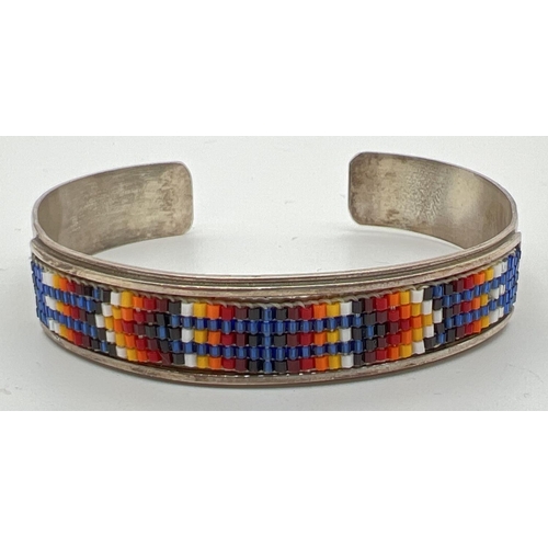 1009 - A Native American silver bangle with multi coloured small glass bead work panel set to front. Makers... 