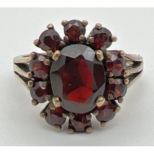 1094 - A vintage silver cocktail style ring set with Garnets. oval cut central garnet surrounded by 10 smal... 