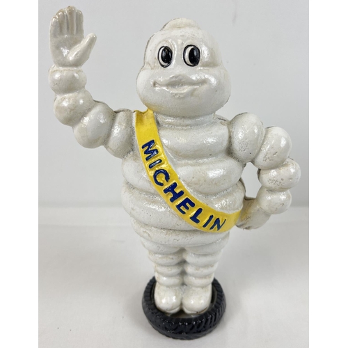 1323 - A painted cast iron money bank of a waving Michelin man stood on a tyre. Approx. 22cm tall.