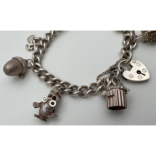 1114 - A vintage silver charm bracelet with padlock and safety chain. Complete with 8 silver and white meta... 