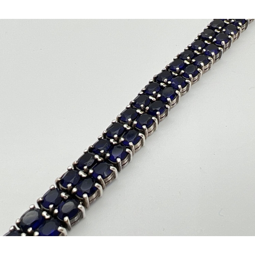 1169 - A double row tennis style silver bracelet set with oval cut dark blue glass stones. Approx 7.5 inche... 