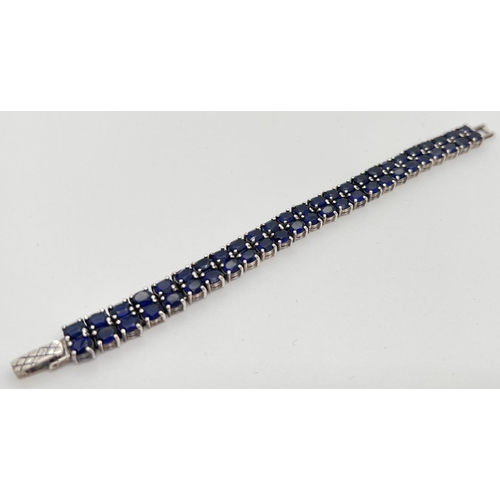 1169 - A double row tennis style silver bracelet set with oval cut dark blue glass stones. Approx 7.5 inche... 