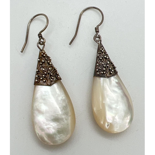 1192 - A pair of mother of pearl teardrop earrings with silver caps and posts, floral decoration to caps wi... 