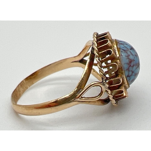 1194 - A vintage 18ct gold dress ring set with a round cabochon of blue and maroon speckled glass. Frilled ... 