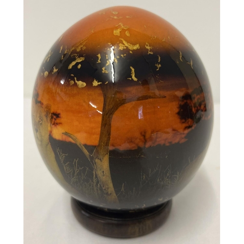 1370 - A painted and lacquered African Ostrich egg with lions at sunset scene and gold fleck detail with a ... 