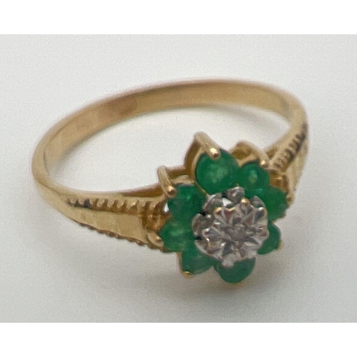 23 - An unmarked 9ct gold, emerald and diamond ring in a flower shaped setting with decorative shoulders.... 