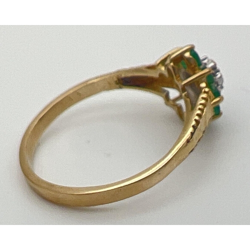 23 - An unmarked 9ct gold, emerald and diamond ring in a flower shaped setting with decorative shoulders.... 