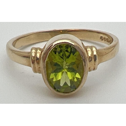 64 - A modern 9ct gold ring with an oval bezel set peridot and ridged design to shoulders. Fully hallmark... 