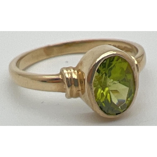 64 - A modern 9ct gold ring with an oval bezel set peridot and ridged design to shoulders. Fully hallmark... 