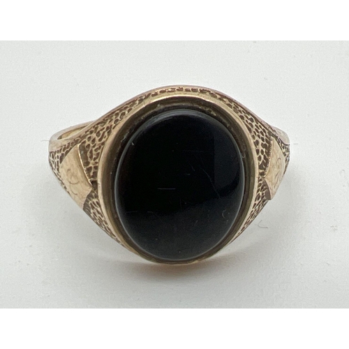 1025 - A mens 9ct gold vintage signet ring set with an oval black onyx stone. Pitted effect detail to shoul... 