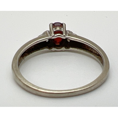 1083 - A 9ct white gold dress ring set with garnets and diamonds. A central oval cut garnet with 3 small ro... 