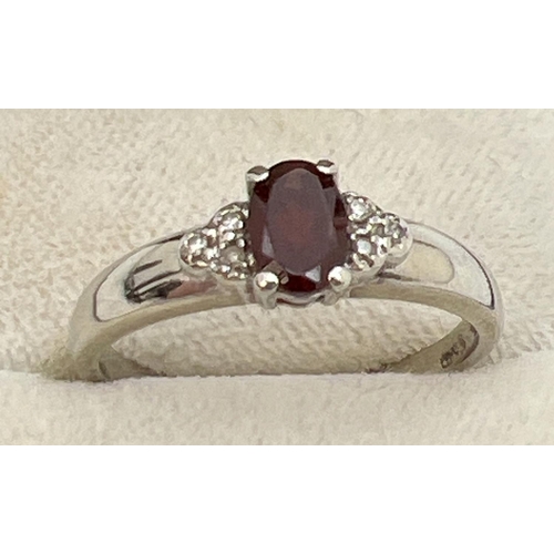 1083 - A 9ct white gold dress ring set with garnets and diamonds. A central oval cut garnet with 3 small ro... 