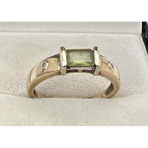 1087 - A 9ct gold modern design dress ring set with a central baguette cut peridot stone with a small round... 