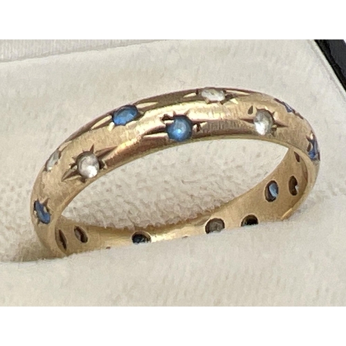 1088 - A 9ct gold band ring set with blue and clear stones. Design cut into ring around each stone to make ... 