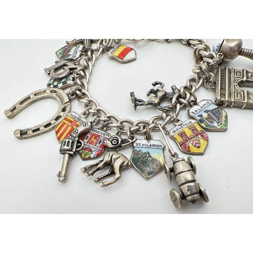 1099 - A vintage curb chain charm bracelet with 24 silver and white metal charms. To include a car, gun, ho... 