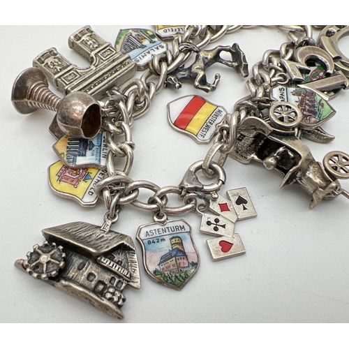 1099 - A vintage curb chain charm bracelet with 24 silver and white metal charms. To include a car, gun, ho... 