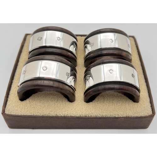 1144 - A boxed set of 4 dark wood napkin rings with hallmarked silver banded detail. Each approx. 4.5cm dia... 