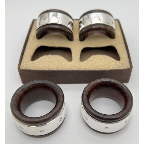 1144 - A boxed set of 4 dark wood napkin rings with hallmarked silver banded detail. Each approx. 4.5cm dia... 