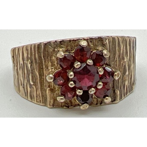 1023 - A vintage 9ct yellow gold ring with textured bark effect band set with a cluster of garnets in a flo... 