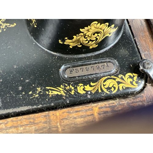 1304 - An antique wooden cased Singer sewing machine, black with gold floral decoration and shuttle bobbin.... 