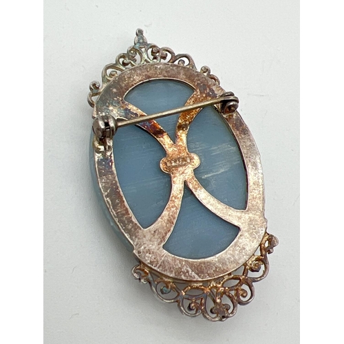 1026 - A vintage classic style blue cameo brooch in a decorated pierced work mount. Marked silver to back. ... 