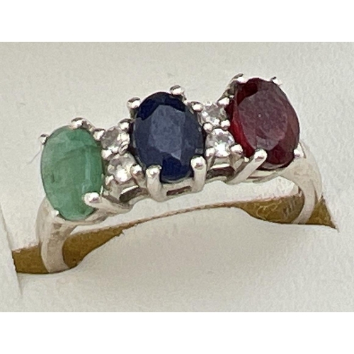 38 - A silver trilogy dress ring set with oval cut emerald, sapphire & ruby interspersed with 4 small dia... 