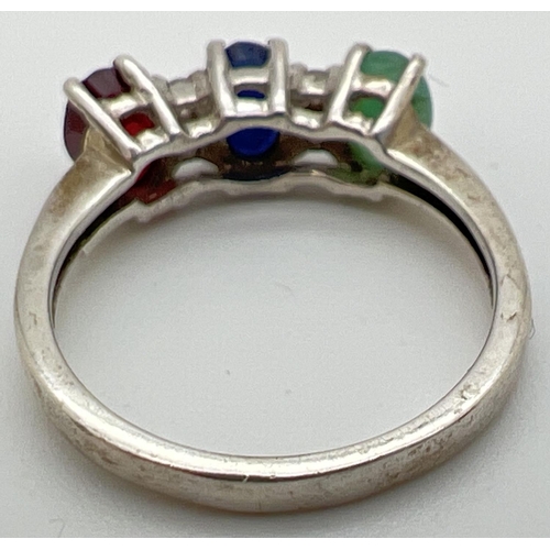 38 - A silver trilogy dress ring set with oval cut emerald, sapphire & ruby interspersed with 4 small dia... 