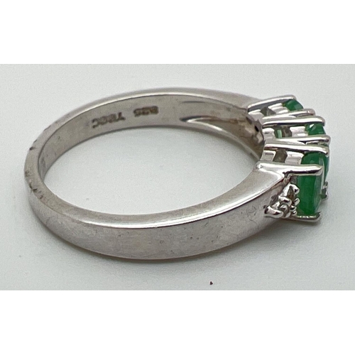 59 - A Genuine Gem Company silver and emerald trilogy ring with diamond clusters set to each shoulder. In... 