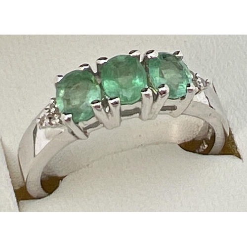 59 - A Genuine Gem Company silver and emerald trilogy ring with diamond clusters set to each shoulder. In... 