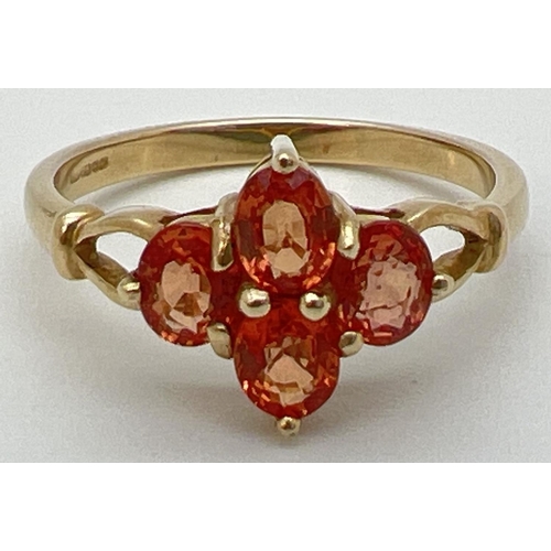 77 - A 9ct gold and orange sapphire ring with a quatrefoil shaped setting and open design shoulders. Full... 