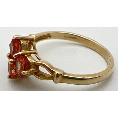 77 - A 9ct gold and orange sapphire ring with a quatrefoil shaped setting and open design shoulders. Full... 