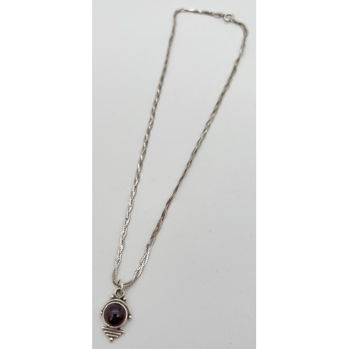 100 - An Art Deco design pendant set with a circular cabochon of garnet, on a 16