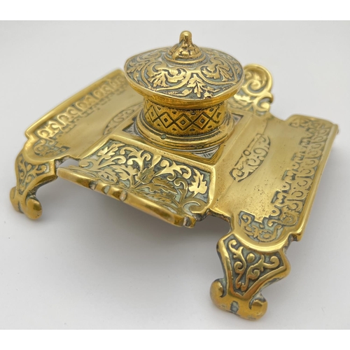 1158 - An antique brass inkwell with decorative scroll & foliate design to pen tray. Stamped '310' to under... 