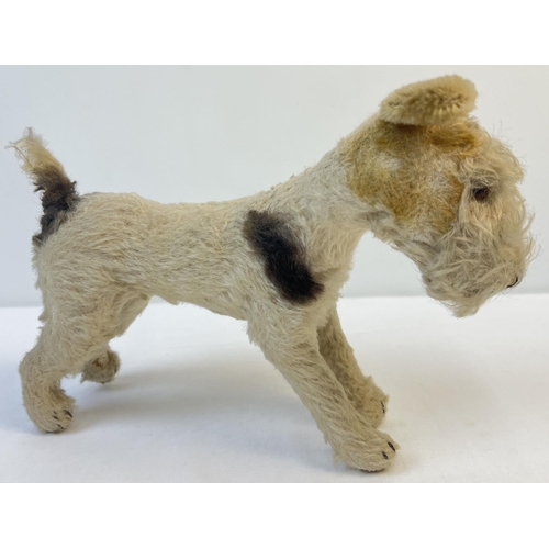 A vintage mohair, straw filled fox terrier dog with working squeaker in tummy. Nylon haired ears, plastic eyes and stitched nose and mouth. Pads are worn - one has a hole and filling & wire rod is visible. Hair is worn in areas. Approx. 19.5cm tall x 26cm long.