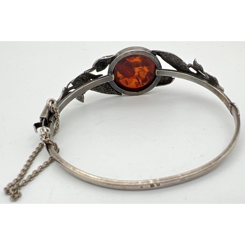 1001 - A silver bangle style bracelet set with a round cut piece of cognac amber with leaf design to both s... 