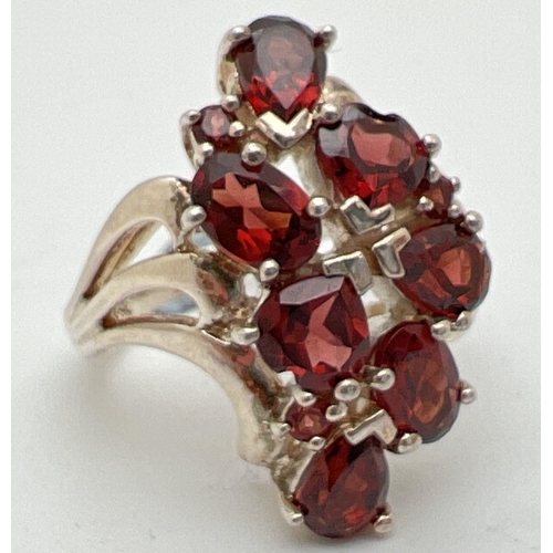 1060 - A silver statement dress ring set with teardrop, round, oval and heart shaped garnet stones. Swirl d... 